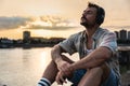 Happy teenage male tourist sitting on sea promenade of an old city in sunset. Young man world traveler singing his favorite song