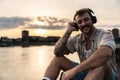 Happy teenage male tourist sitting on sea promenade of an old city in sunset. Young man world traveler singing his favorite song