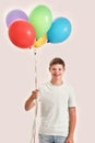 Happy teenaged disabled boy with Down syndrome smiling at camera, holding a bunch of colorful balloons while standing Royalty Free Stock Photo