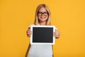 Happy teenager blonde lady schoolgirl in glasses shows tablet with blank screen, recommends new app