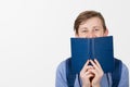 Happy teenager boy smiling covering half face with a opened blue book. Book lover. Ready to study hard.