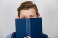 Happy teenager boy smiling covering half face with a opened blue book. Book lover. Ready to study hard Royalty Free Stock Photo