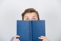 Happy teenager boy  smiling and looking up having new ideas covering half face with a opened blue book. Book lover. Ready to study Royalty Free Stock Photo