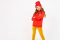 Happy teenager girl with red hair, red hat, hoody and yellow trousers smiles and drinks coffee isolated on white Royalty Free Stock Photo