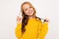 Happy teenager girl with red hair, hoody and yellow trousers holds contact lenses and glasses isolated on white Royalty Free Stock Photo