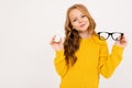 Happy teenager girl with red hair, hoody and yellow trousers holds contact lenses and glasses isolated on white Royalty Free Stock Photo