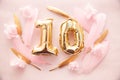 Happy tenth birthday with golden number ten 10 and feathers with colorful decorations on pink