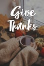 Happy Thanksgiving! Give thanks text and hands in sweater holding warm cup of tea with stylish pumpkins and fall leaves. Season