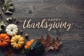 Happy Thanksgiving greeting text with pumpkins, squash and leaves over dark wood background