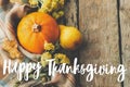 Happy thanksgiving text on pumpkin, autumn leaves, flowers, pears, cozy blanket on rustic old wood. Seasonal greeting card,