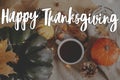 Happy Thanksgiving! Happy thanksgiving text and warm cup of tea, pumpkins, fall leaves, cozy scarf and lights on rustic table. Royalty Free Stock Photo