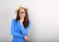 Happy thinking young woman looking up in fashion glasses and straw hat on blue background