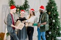 Happy three Caucasian women, Caucasian man and African man holding Christmas presents at home. Christmas tree Royalty Free Stock Photo