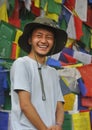 A happy tibetan young man looking sideways, standing against Buddhist prayer flags