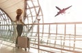 Happy time young tourist woman holding the luggage and watching the flight and sunlight through window in Airport