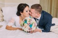 Happy tired newlyweds lay on bed in hotel room after wedding celebration and share kiss