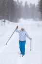 Happy and tired woman running on ski on forest road at strong blizzard and greeting with poles Royalty Free Stock Photo
