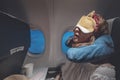 Tired young woman comfortably sleeping with mask and pillow in airplane. Sophisticated traveler concept