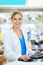 Happy to assist you. a young pharmacist using a computer at the checkout counter.