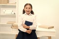 Happy to enter into first form. Girl child holds book stand near table white background. Schoolgirl enjoy studying and