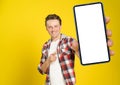 Happy to win handsome man pointing at smartphone with white empty screen, wearing red plaid shirt and jeans cellphone Royalty Free Stock Photo