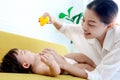 Happy toddle baby lying on yellow sofa in living room, mom holding duck toy for playing with little girl daughter, parent play Royalty Free Stock Photo