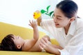 Happy toddle baby lying on yellow sofa in living room, mom holding duck toy for playing with little girl daughter, parent play Royalty Free Stock Photo