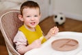 Happy toddler baby boy eating apple pieces while sitting on a high chai Royalty Free Stock Photo