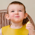 Happy toddler baby boy eating apple pieces while sitting on a high chai Royalty Free Stock Photo