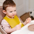 Happy toddler baby boy eating apple pieces while sitting on a high chai Royalty Free Stock Photo