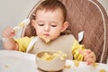 Happy toddler baby boy learns to eat porridge himself with a spoon wh Royalty Free Stock Photo