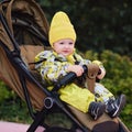 Happy toddler baby boy in yellow overalls sits in a stroller. A child in wa Royalty Free Stock Photo