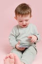 Happy toddler baby with mobile phone on studio pink background. Child boy holding a smartphone in his hands. Kid age one year Royalty Free Stock Photo