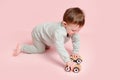 Happy toddler baby is playing with a toy car against a pink background Royalty Free Stock Photo