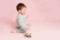 Happy toddler baby is playing with a toy car against a pink background Royalty Free Stock Photo