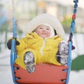 Happy toddler baby rides on a swing on a winter playground. Baby boy Royalty Free Stock Photo