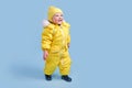 Happy toddler baby in winter clothes snowsuit on studio blue background. A child in a warm yellow jumpsuit with a hood. Kid aged Royalty Free Stock Photo