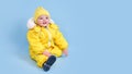 Happy toddler baby in winter clothes snowsuit on studio blue backgrou