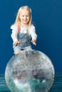 Happy toddler blonde girl havig fun while rolling giant disco ball on the floor