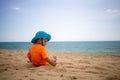 A happy toddler in blue hat and orange t-sirt plays sand on a tropical beach and picking on the sand. sea is on Royalty Free Stock Photo