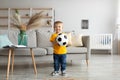 Happy toddler boy football fan posing with soccer ball and smiling at camera, having fun at home in living room Royalty Free Stock Photo