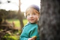 A happy toddler boy hiding behind tree outside in spring nature. Royalty Free Stock Photo