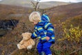 Happy toddler child, holding teddy bear, posing in front of beautiful waterfal Svartifossl in Skaftafell national park in Iceland Royalty Free Stock Photo