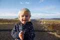 Happy toddler child, smiling, posing for camera, standing on a little path, lighthouse behind him, Iceland