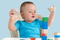 Happy toddler 12-17 months old builds a tower of colorful wooden cubes sitting on a child`s chair Royalty Free Stock Photo