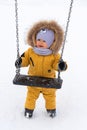 A happy toddler 12-17 months old in yellow winter clothes is holding onto a swing and trying to swing on them. A baby on a Royalty Free Stock Photo