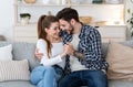 Happy together at home. Glad young man and woman in casual clothes are holding hands, hugging on sofa Royalty Free Stock Photo