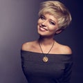 Happy toothy smiling woman with short blond bob hairstyle in grey blouse and orange fashion necklace on gray background. Closeup Royalty Free Stock Photo