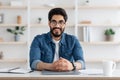 Happy toung arab self-entrepreneur man sitting at desk in home office interior and smiling to camera Royalty Free Stock Photo