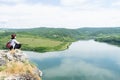 Happy Tourist caucasian white girl with red hat alone sitting on wild national park, enjoying the view of a lake and a forest. Royalty Free Stock Photo